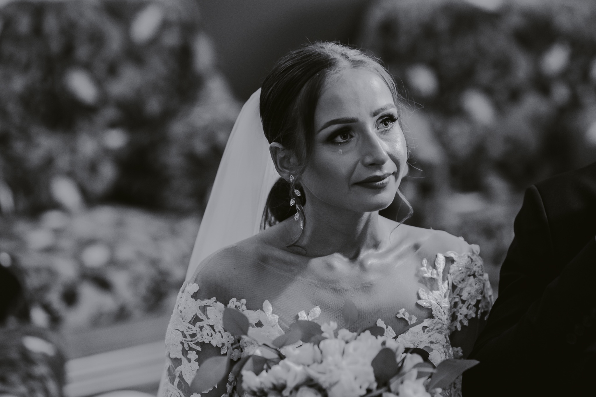 Czarno-białe ujęcie panny młodej w Złoczewie, z bukietem i welonem, spoglądającej w bok z lekkim uśmiechem i łzą w oku.