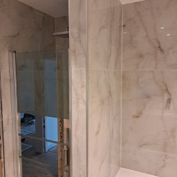 ROB-BUD Prestige wykończenia wnętrz Robert Makowski - Wykończona łazienka z beżowymi płytkami imitującymi marmur, kabina prysznicowa ze srebrnym uchwytem, widoczny fragment wanny.