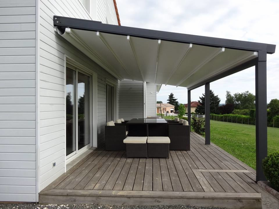 Nowoczesna altana z rozsuwanym zadaszeniem i ciemnymi meblami ogrodowymi na drewnianym tarasie przylegającym do domu o białej elewacji.