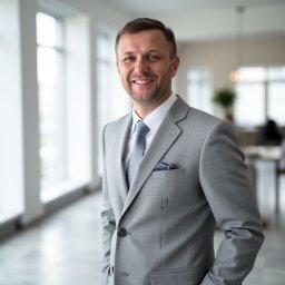 Biuro Rachunkowe Gusto Sp. z o.o. - Uśmiechnięty mężczyzna w szarym garniturze, Krosno Odrzańskie. Portret biznesowy w jasnym biurze, z chusteczką w kieszonce i subtelnym logo na klapie.