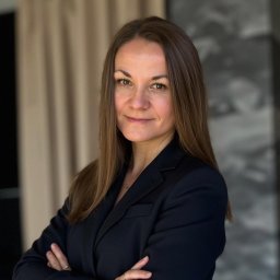 Biuro Rachunkowe Gusto Sp. z o.o. - Profesjonalny portret kobiety w czarnym żakiecie, z założonymi rękami, na neutralnym tle. Uśmiech, długie włosy, subtelna biżuteria.