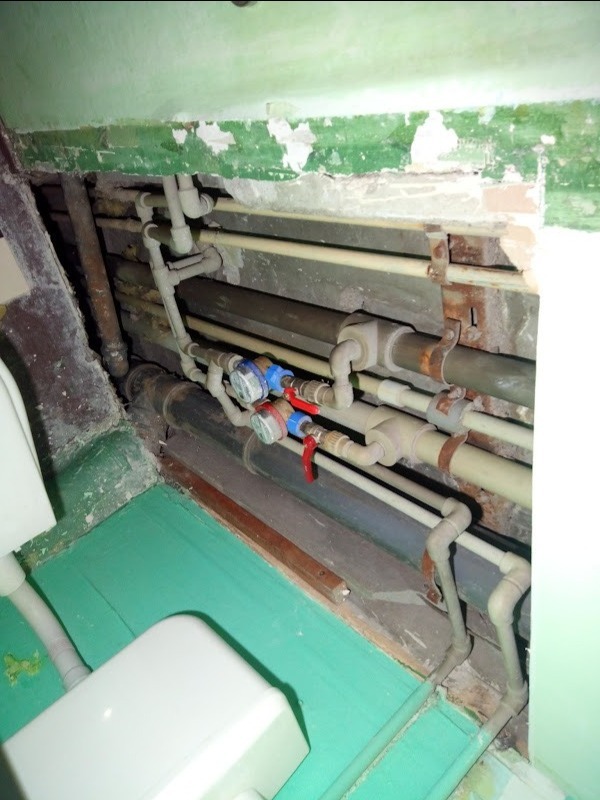 Rury wodne i zawory w starej łazience we Wrocławiu, widoczne ślady korozji na wspornikach i odpryski farby na ścianie.