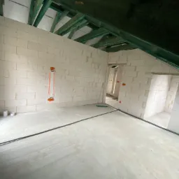 Surowy stan poddasza z widocznymi przewodami elektrycznymi ułożonymi wzdłuż ścian i na podłodze, przygotowane do dalszych prac instalacyjnych.