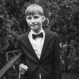 Michał Ciepielowski Dziki kadr - Czarno-białe zdjęcie elegancko ubranego chłopca w Łodzi, w garniturze i muszce, opierającego się o metalową barierkę na tle zieleni. Ujęcie portretowe.