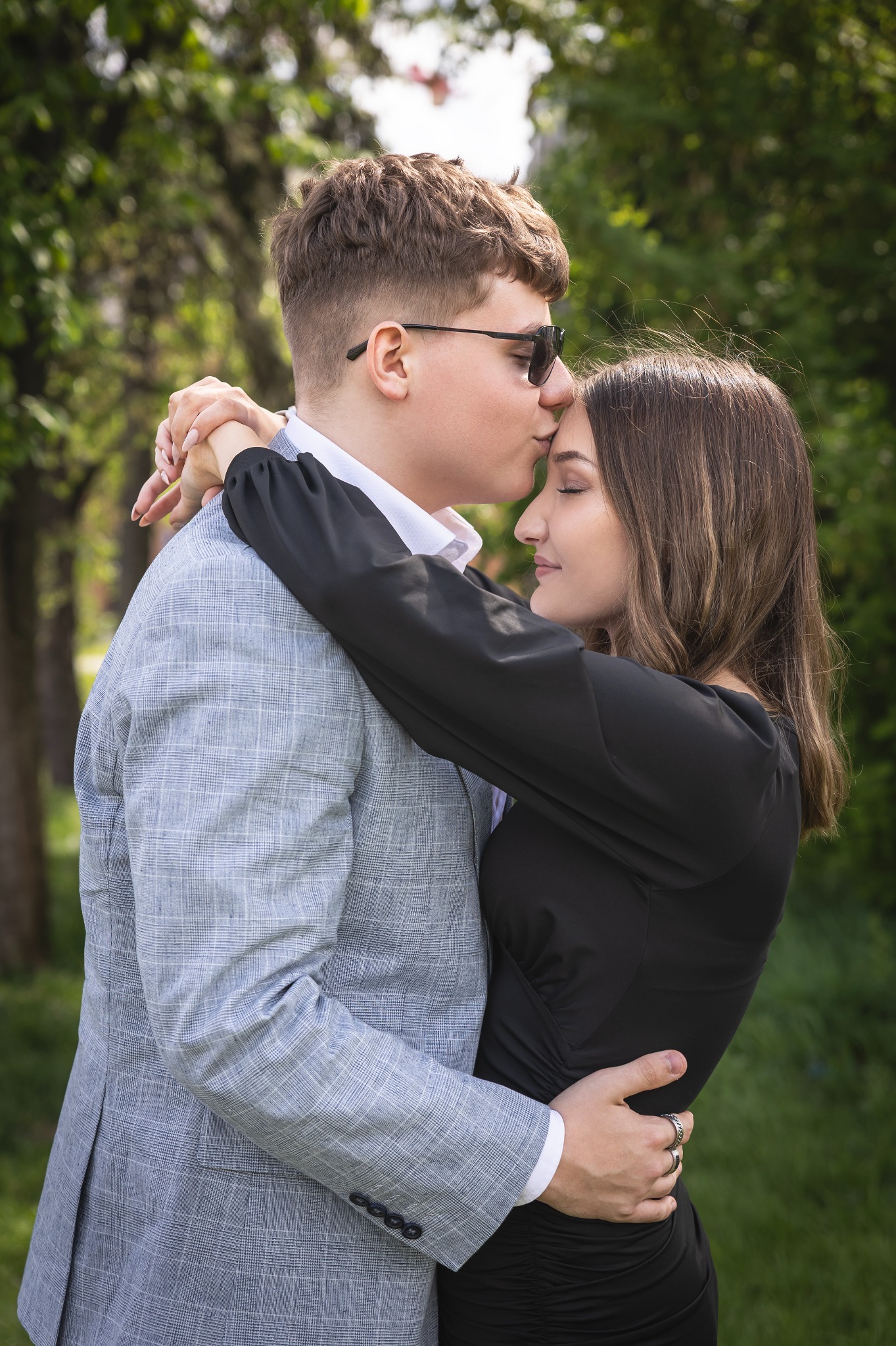 Para zakochanych: mężczyzna w okularach całuje kobietę w czoło. Ujęcie w plenerze, zieleń w tle. Romantyczna chwila, delikatne światło.