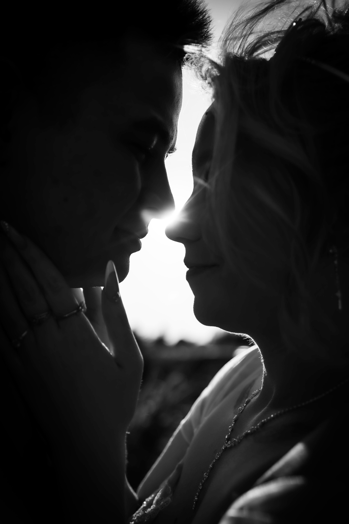 Silhouettes of a couple in a close embrace, sun shining between their faces. Black and white portrait with focus on the connection and intimacy.