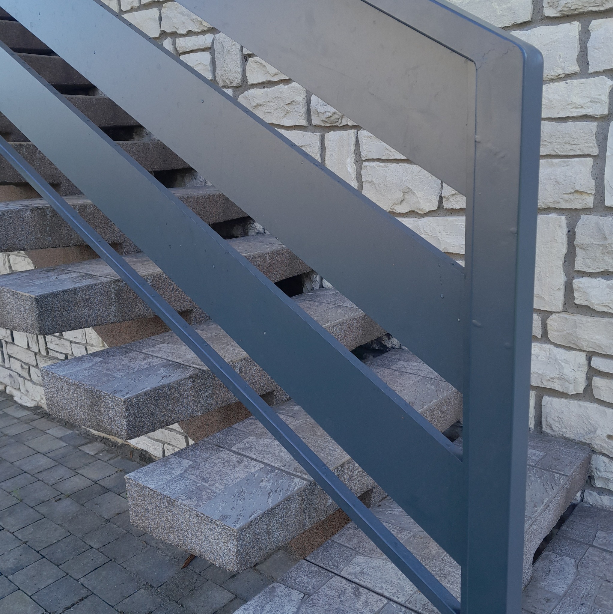 Zewnętrzne schody z metalową balustradą w kolorze grafitowym, prowadzące do kamiennego muru.