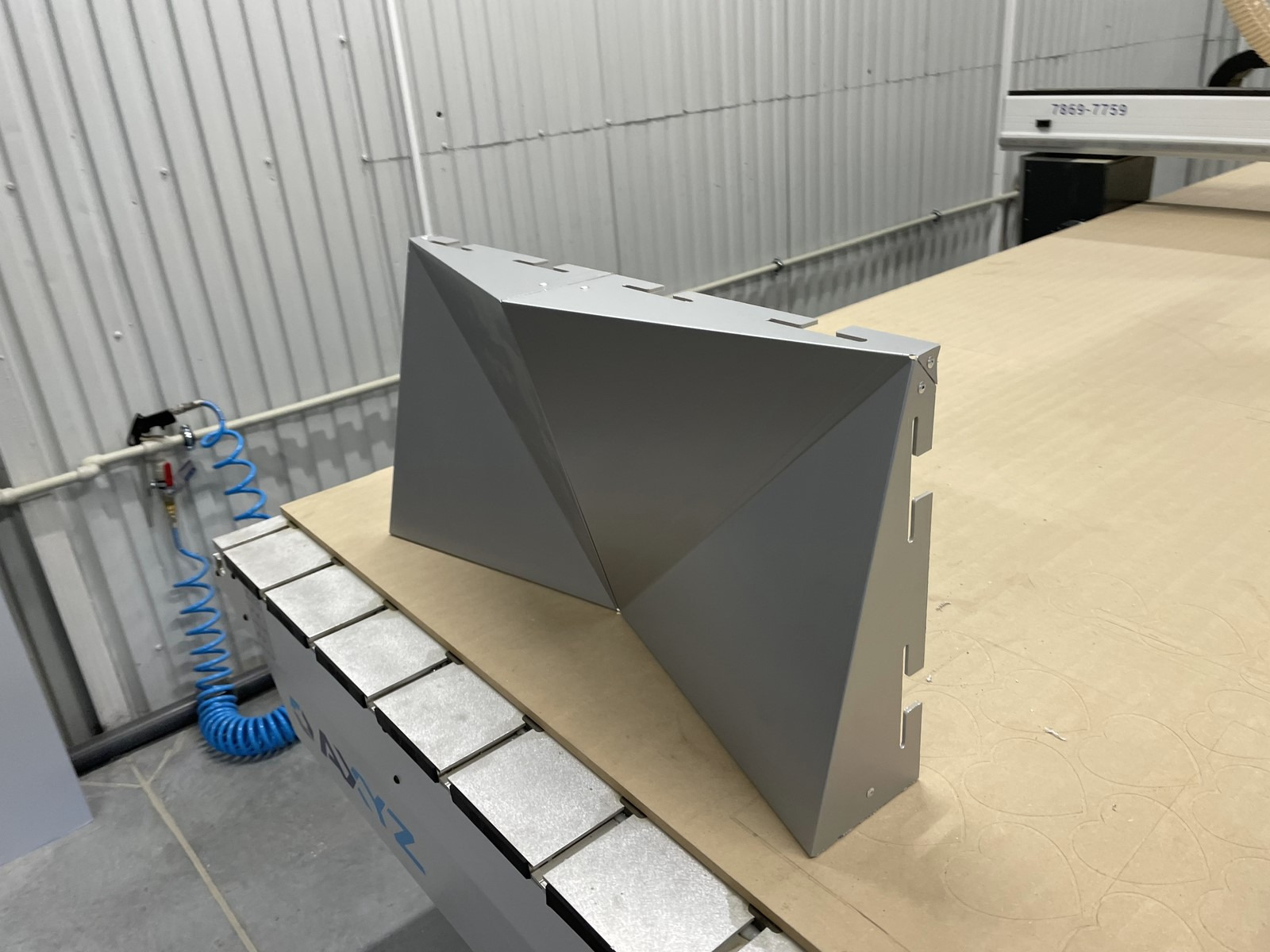 Szary, geometryczny element metalowy, prawdopodobnie obudowa, po obróbce na maszynie CNC w Krakowie. Widoczne ślady mocowania i otwory montażowe.