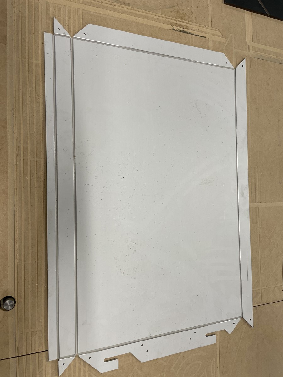 Płyta aluminiowa z wycięciami na krawędziach, potencjalny element konstrukcyjny, leżąca na powierzchni roboczej.