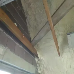 Ocieplenie poddasza pianką PUR między drewnianymi krokwiami, widoczne fragmenty murowanej ściany z pustaków.