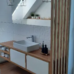 Nowoczesna łazienka na poddaszu z drewnianym blatem pod umywalkę nablatową, białymi frontami szafek, dekoracyjną ścianą z płytek 3D i drewnianą ażurową ścianką działową.