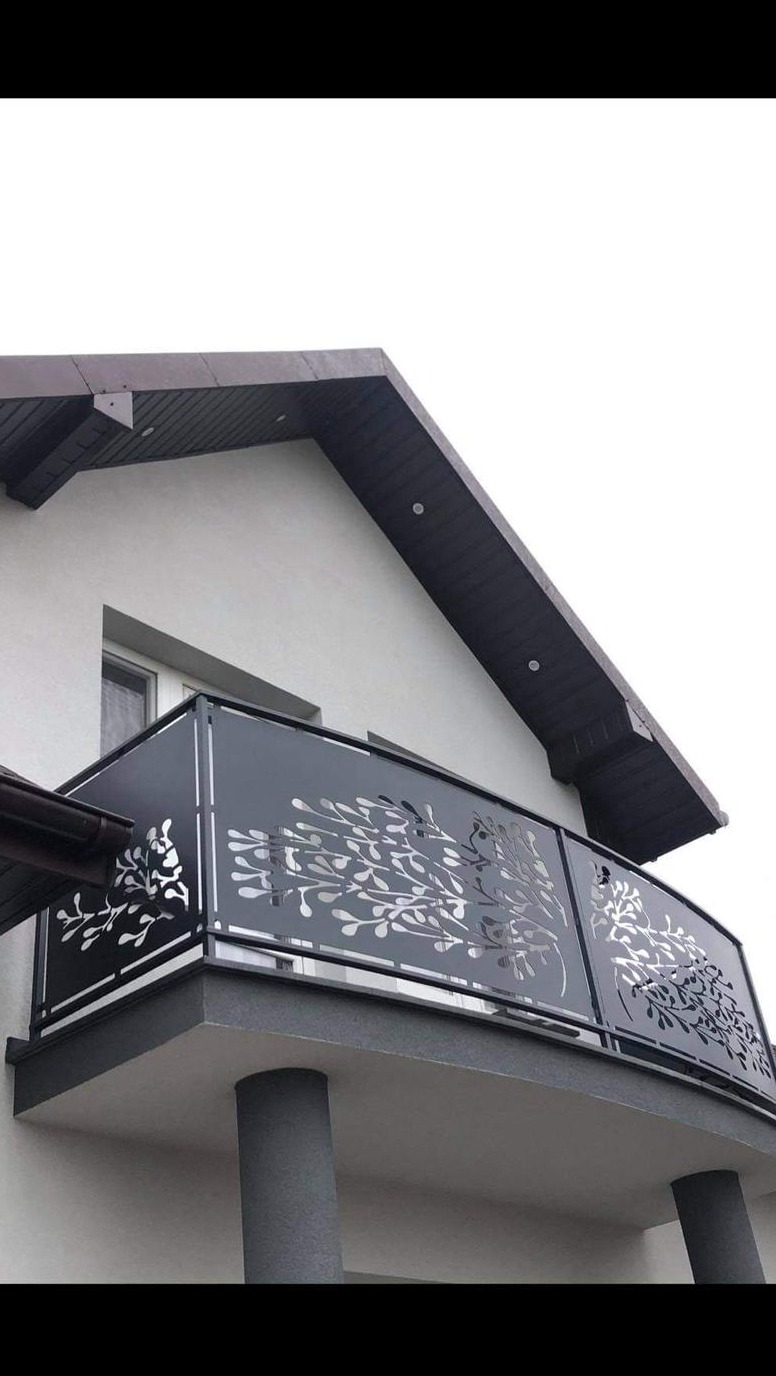 Nowoczesna balustrada balkonowa z ażurowym wzorem roślinnym, zamontowana na budynku z szarą elewacją i ciemnym dachem.