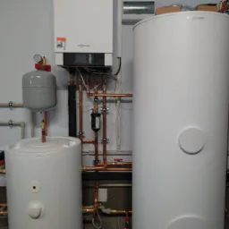 Zestaw urządzeń grzewczych Viessmann: wiszący piec, dwa białe zbiorniki akumulacyjne, szary zbiornik wyrównawczy i miedziana instalacja hydrauliczna z filtrem, zamontowane przy ścianie.