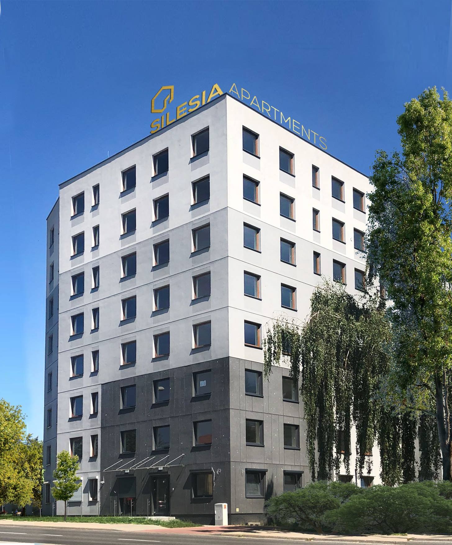 Nowoczesny budynek apartamentowy z elewacją w odcieniach szarości i białym wykończeniem, z logo 'Silesia Apartments' na dachu, otoczony zielenią.