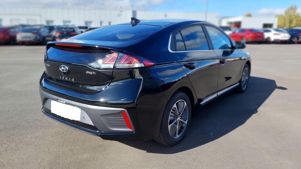 Czarny, błyszczący samochód Hyundai Ioniq Plug-in, widoczny z tyłu pod kątem, zaparkowany na parkingu z innymi samochodami w tle.