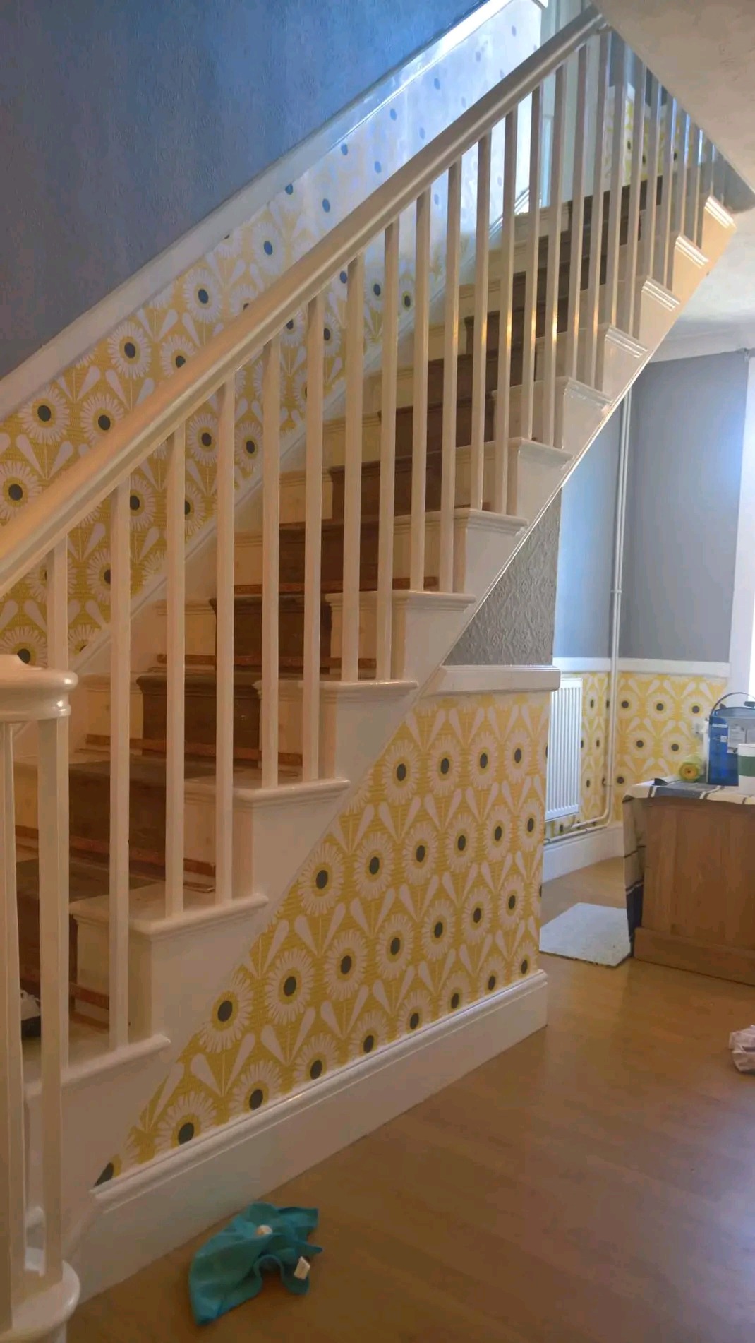 Schody w domu po położeniu tapety w żółto-białe kwiaty, białe balustrady i drewniane stopnie.