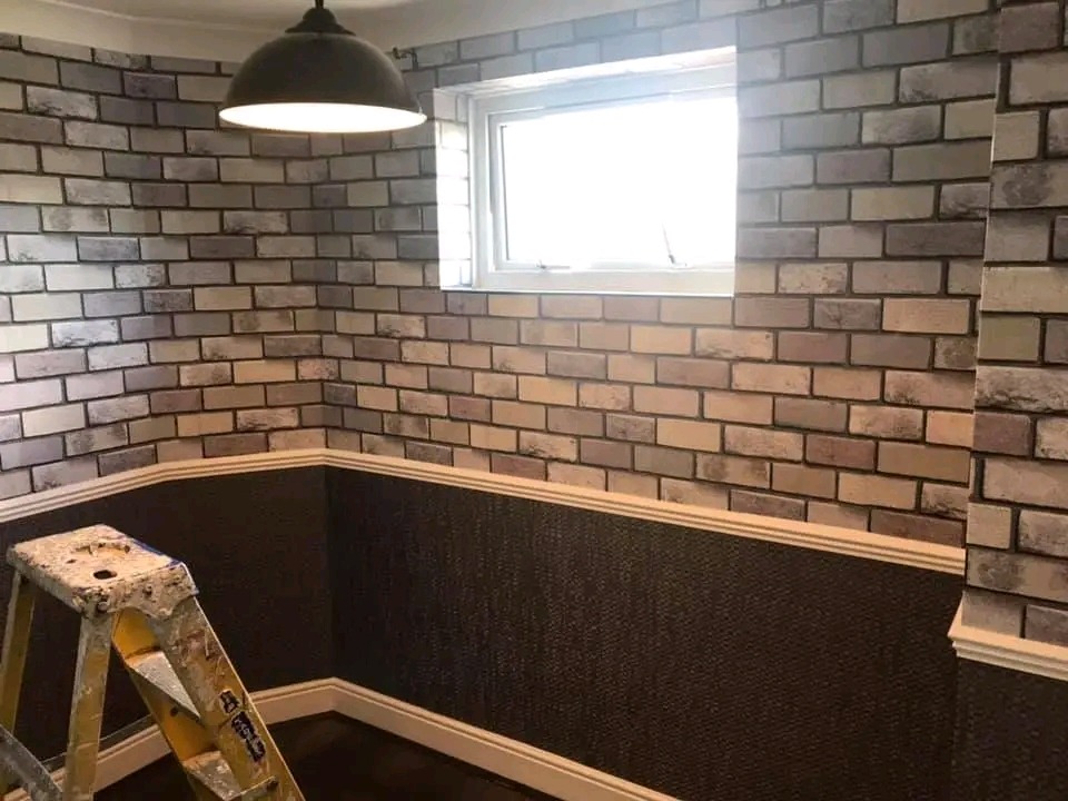 Pokój po remoncie z tapetą imitującą cegłę na górnej części ścian i ciemną tapetą strukturalną w dolnej części, oddzielone listwą dekoracyjną, drabina malarska w rogu.