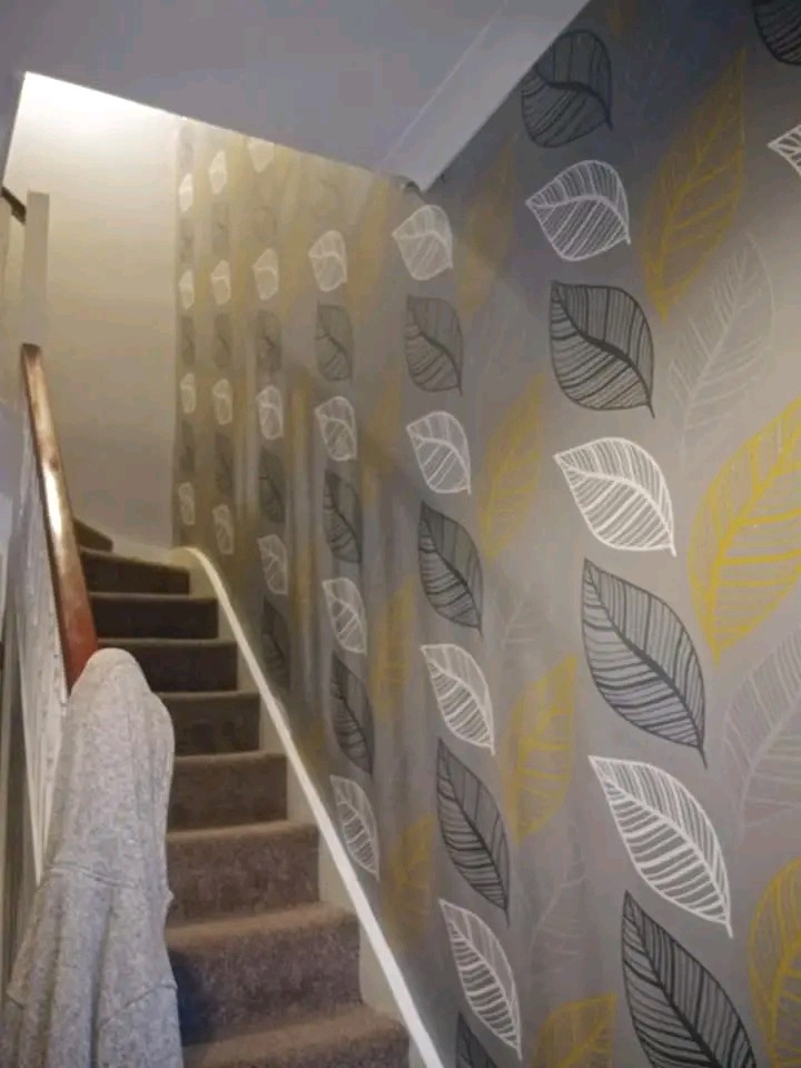 Klatka schodowa z szarą tapetą w liście w odcieniach bieli, szarości i żółci, widok z dołu schodów.