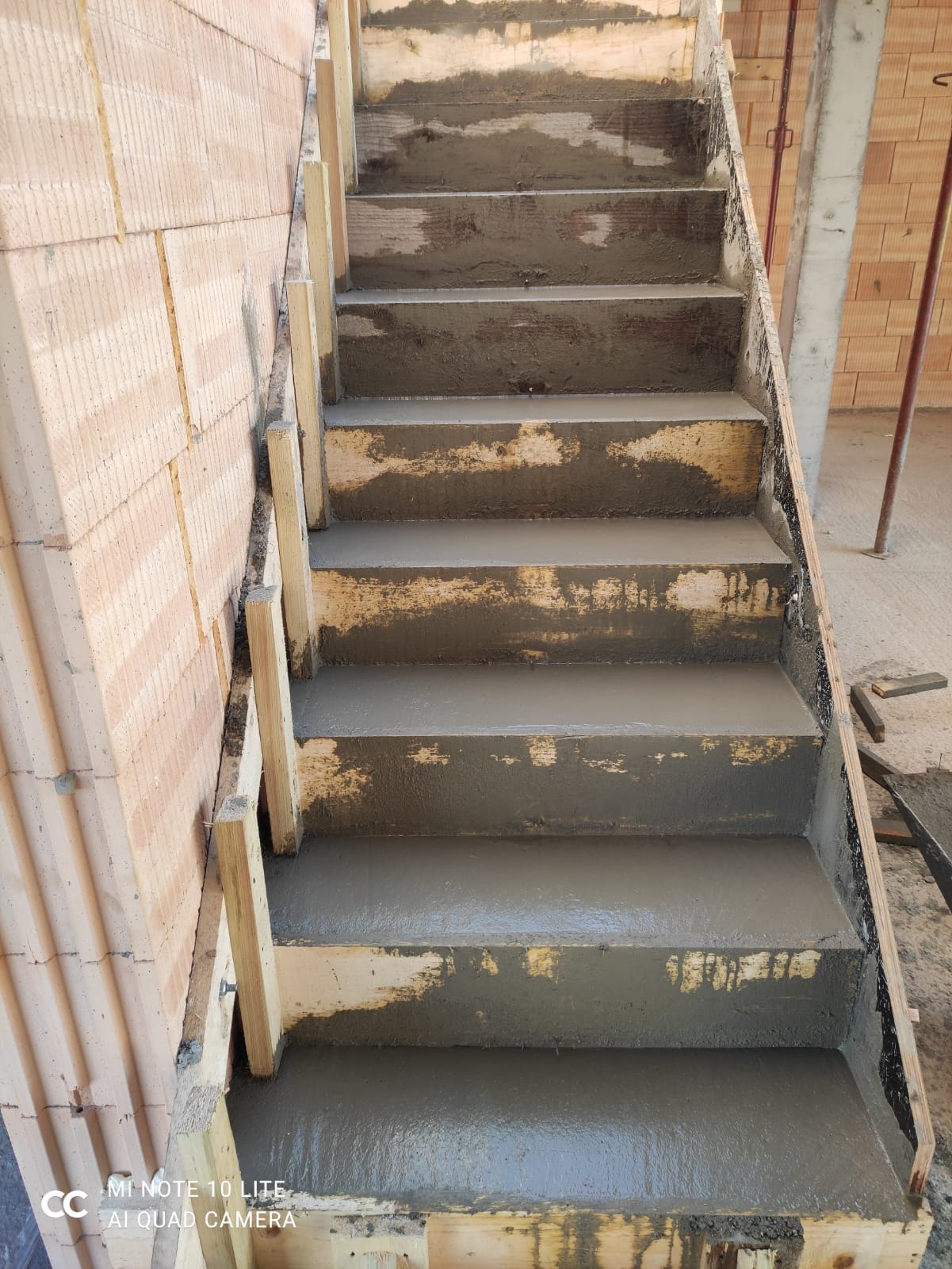 Wewnętrzne schody żelbetowe w trakcie wylewania, widoczne drewniane szalunki i fragment ściany z pustaków ceramicznych.