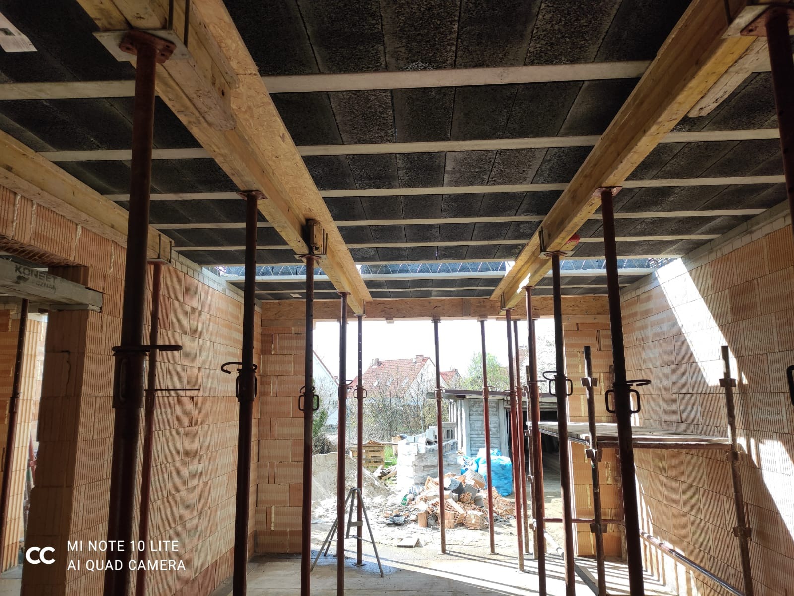 Wnętrze powstającego domu z cegły, widoczne szalunki stropowe podparte metalowymi stemplami, przygotowane do zalewania betonem.