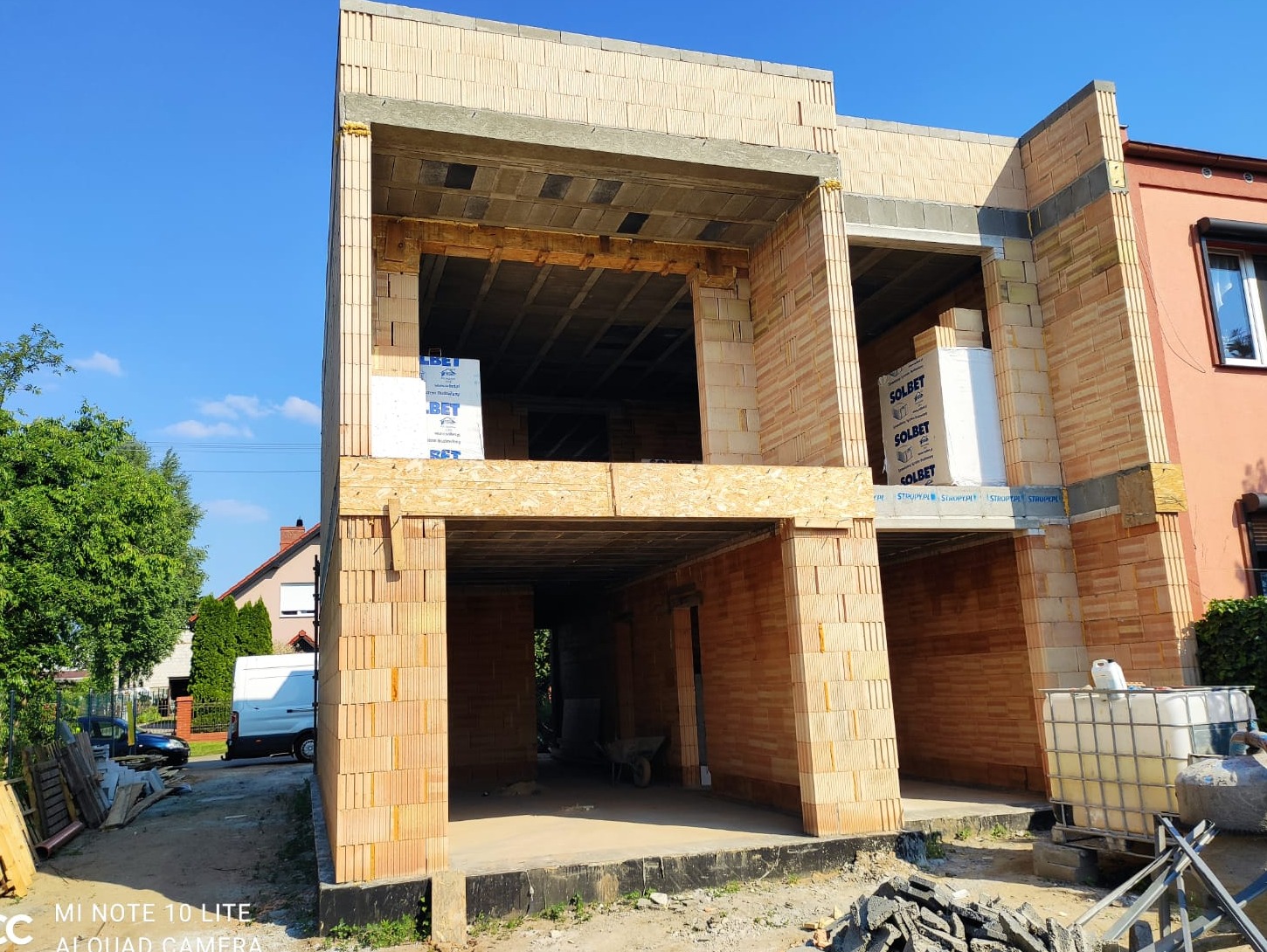 Wznoszony dwukondygnacyjny dom murowany z pustaków ceramicznych, widoczne elementy szalunków, materiały budowlane SOLBET i BET, teren budowy.