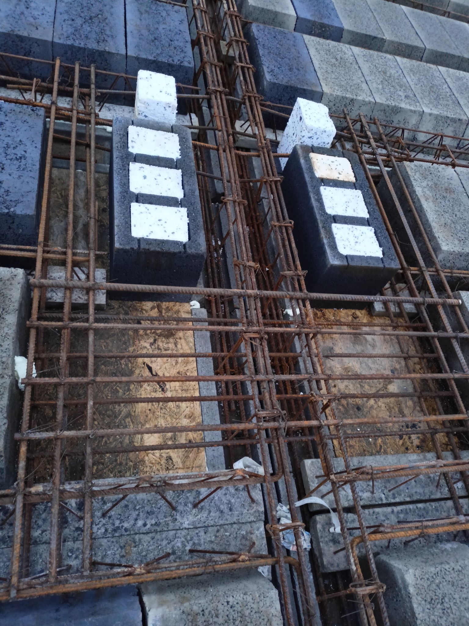 Zbrojenie fundamentu z bloczków betonowych szalunkowych wypełnionych styropianem, widoczne pręty zbrojeniowe i fragmenty styropianu.