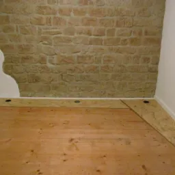 Fragment pokoju w trakcie prac wykończeniowych: drewniana podłoga, fragment ściany z kamienia i gładzi oraz płyta OSB przy ścianie.