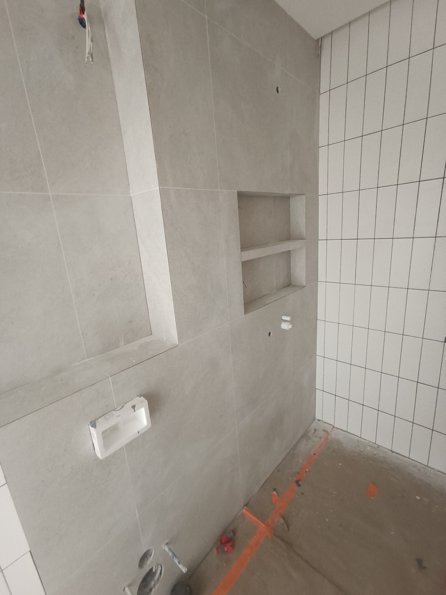 Wnęka z półkami w szarej płytce oraz fragment ściany z białych płytek ułożonych pionowo podczas remontu łazienki.