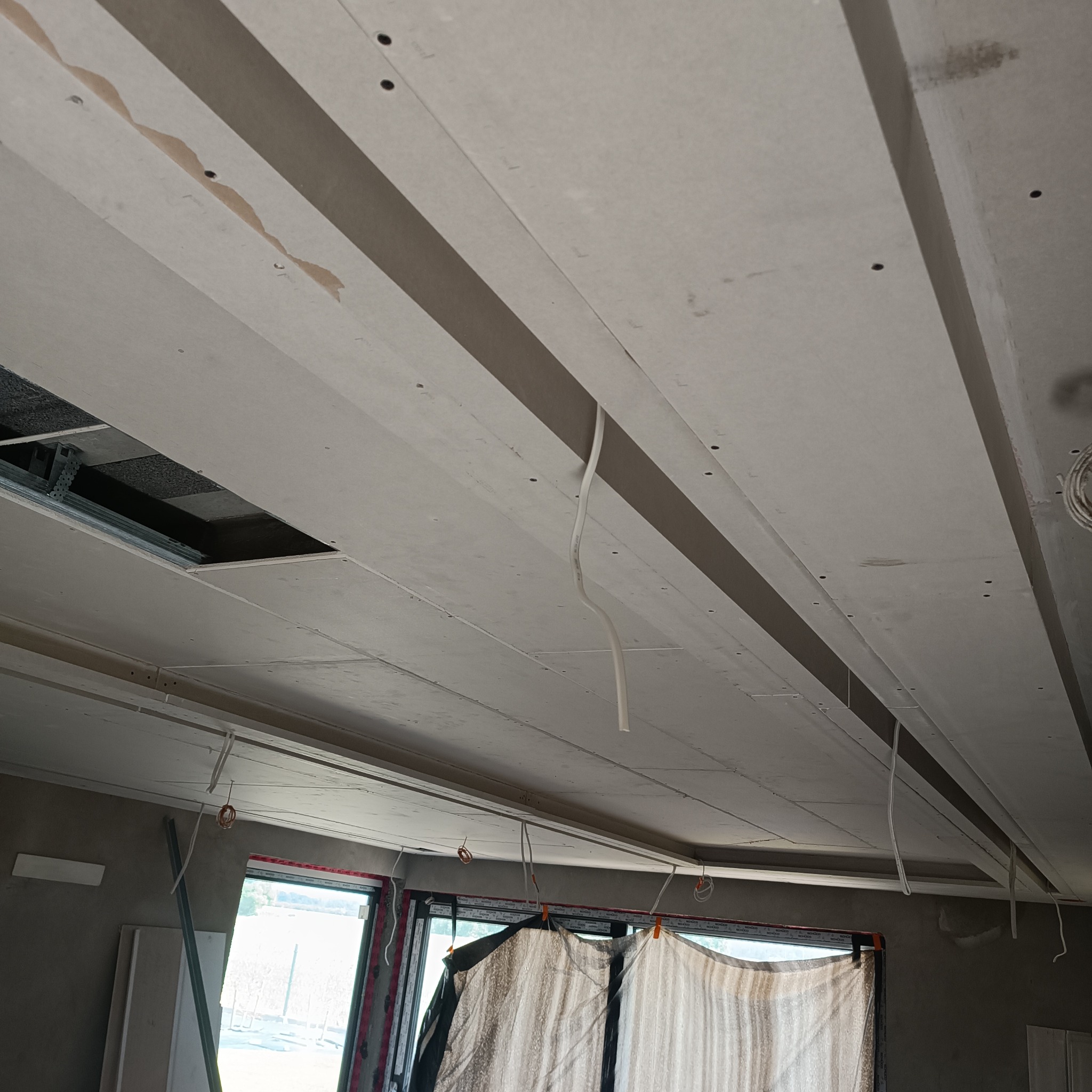 Sufit w trakcie montażu, widoczne płyty z otworami na wkręty, fragment instalacji elektrycznej i metalowa konstrukcja nośna.