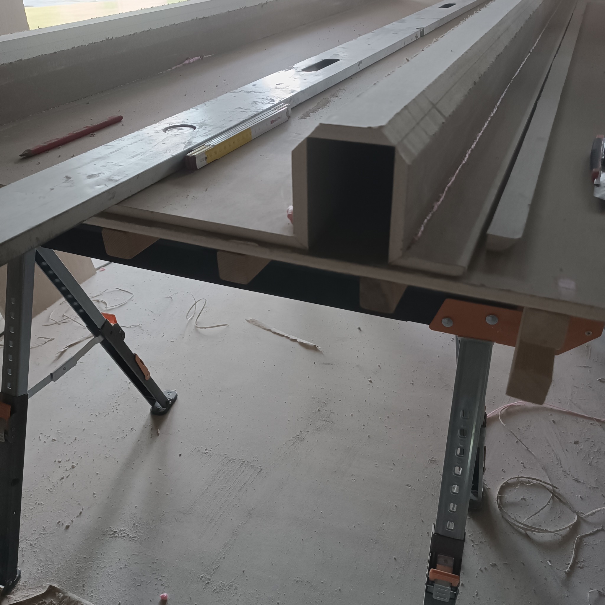 Przygotowane elementy konstrukcyjne z profili, poziomica, miara składana i ołówek na stole roboczym w trakcie prac wykończeniowych.