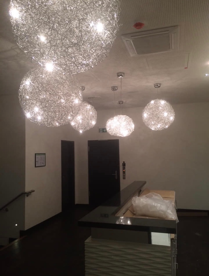 Nowoczesne, kuliste lampy wiszące z metalowej siatki, oświetlające recepcję z ciemną podłogą i jasnymi ścianami w biurze.