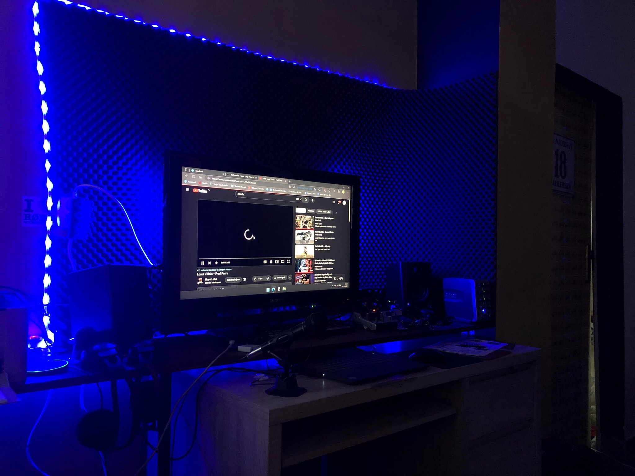 Domowe studio nagrań w Głogowie z ekranem komputera wyświetlającym YouTube, mikrofonem i oświetleniem LED w kolorze niebieskim.