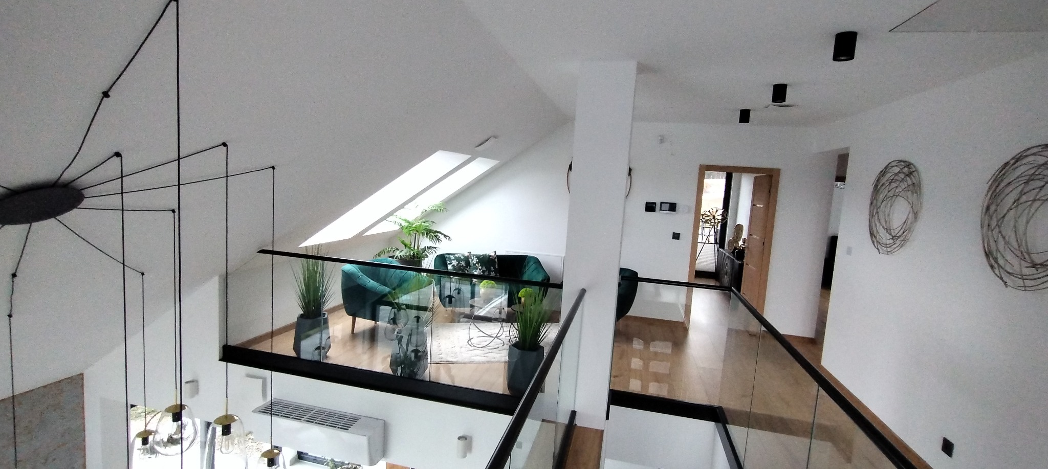 Nowoczesne wnętrze domu z antresolą, szklaną balustradą, zielonymi sofami, dekoracyjnymi lampami pająkami i drewnianą podłogą, widok z góry.