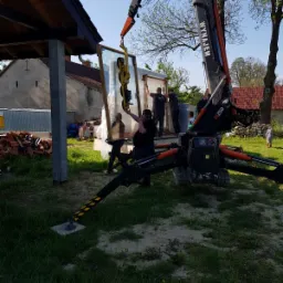 Montaż okna z użyciem dźwigu ssącego, pracownicy w trakcie instalacji, widoczne narzędzia i materiały budowlane w tle.