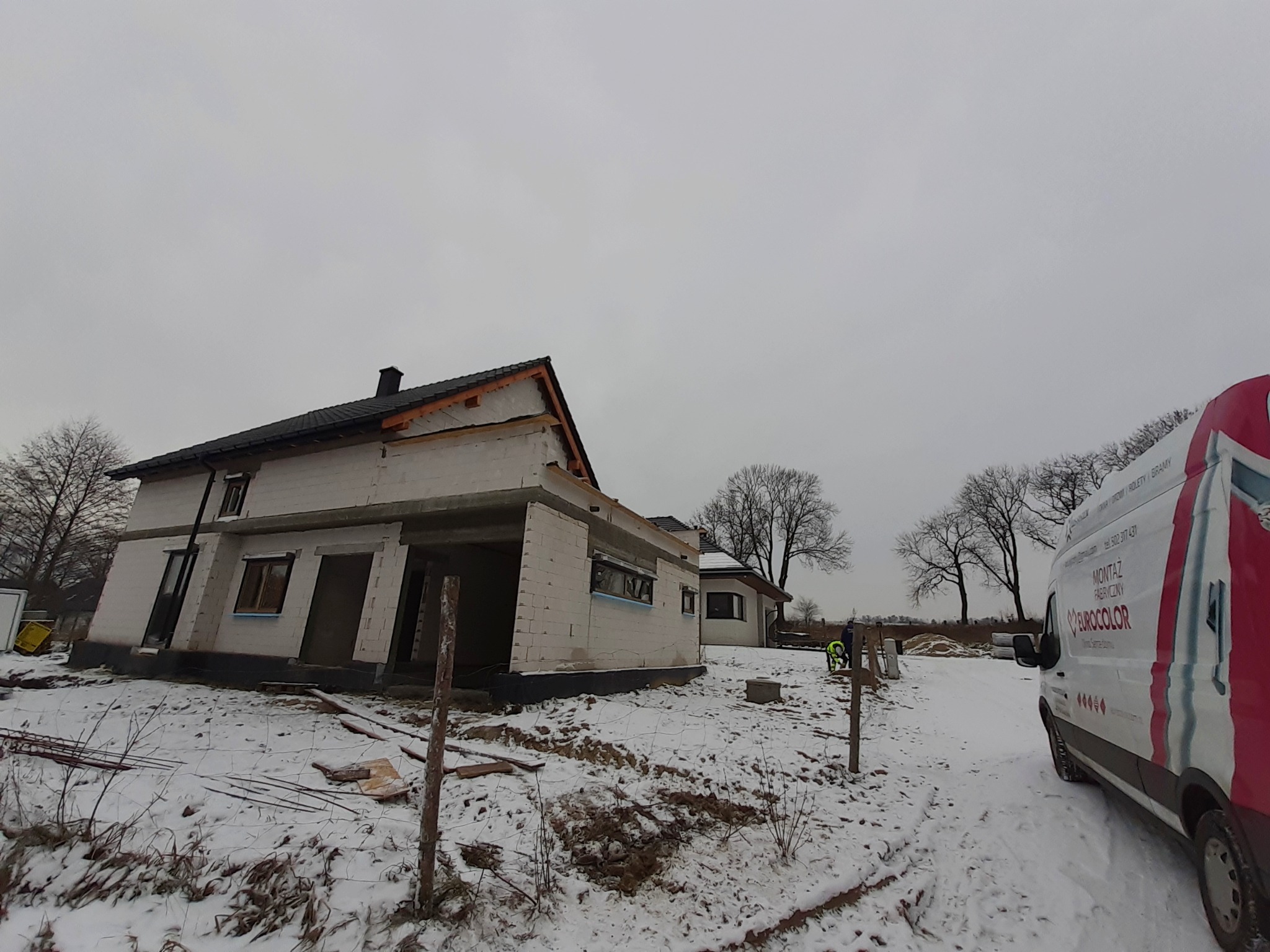 Surowy stan budynku w Zawadzkiem w trakcie montażu stolarki okiennej, widoczny samochód dostawczy z logo firmy na tle zimowego krajobrazu.
