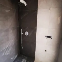 Nowoczesny prysznic walk-in z szarymi płytkami imitującymi marmur, widoczna bateria podtynkowa i deszczownica z zabezpieczeniem.