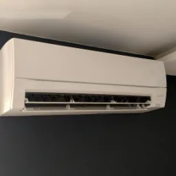 Biała jednostka klimatyzacji Mitsubishi Electric zamontowana na ciemnej ścianie w domu w Józefowie.