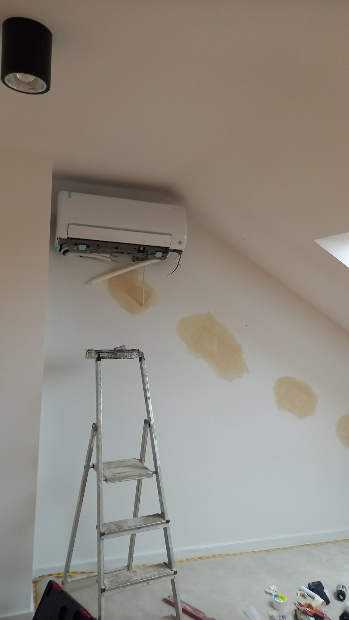 Montaż klimatyzatora na ścianie w pokoju na poddaszu, widoczna drabina i ślady po szpachlowaniu.