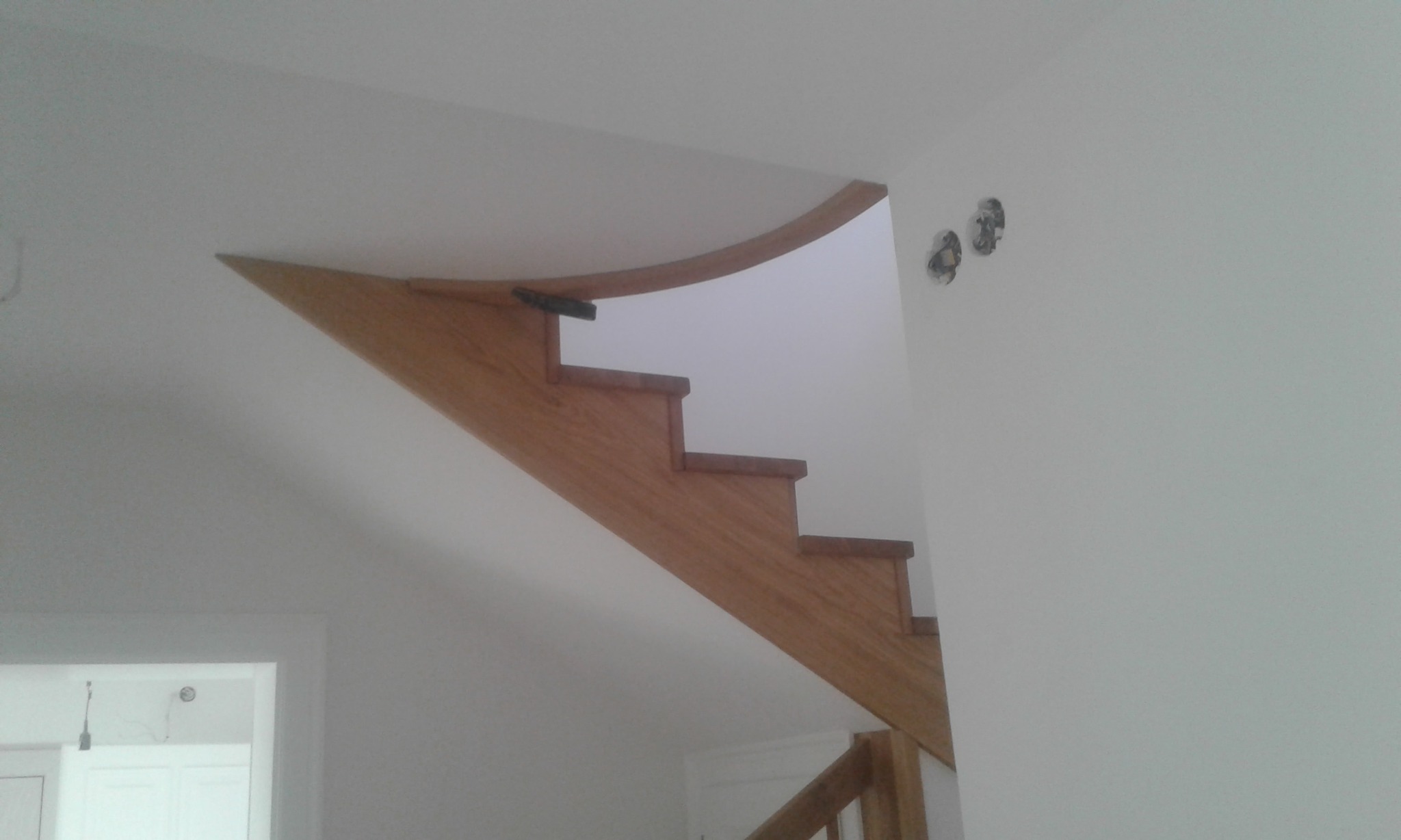 Drewniane schody z balustradą w trakcie montażu, widoczne niedokończone otwory na kontakty elektryczne w ścianie.