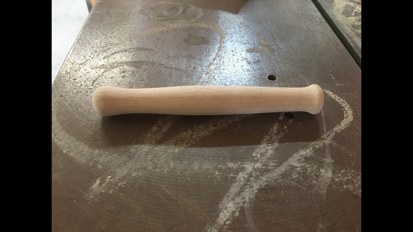 Toczone drewniane ramię uchwytu na warsztatowym stole pokrytym pyłem drzewnym.