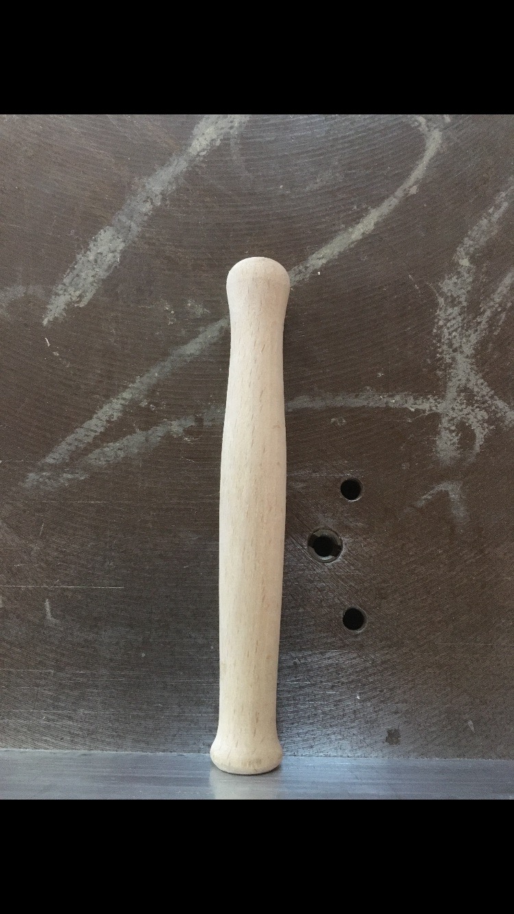 Surowy, toczony uchwyt z jasnego drewna na tle szarego, roboczego stołu z widocznymi śladami obróbki.
