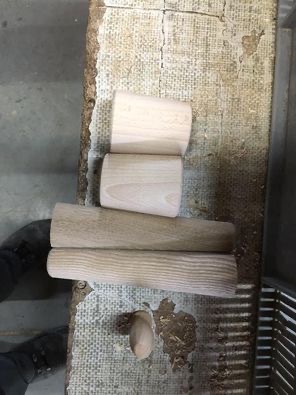 Surowe, drewniane elementy o cylindrycznym kształcie, przygotowane do dalszej obróbki, leżące na roboczym stole z widocznymi śladami użytkowania.