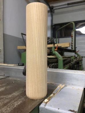 Drewniany, cylindryczny element, prawdopodobnie noga meblowa, na stole warsztatowym z widocznymi śladami obróbki.