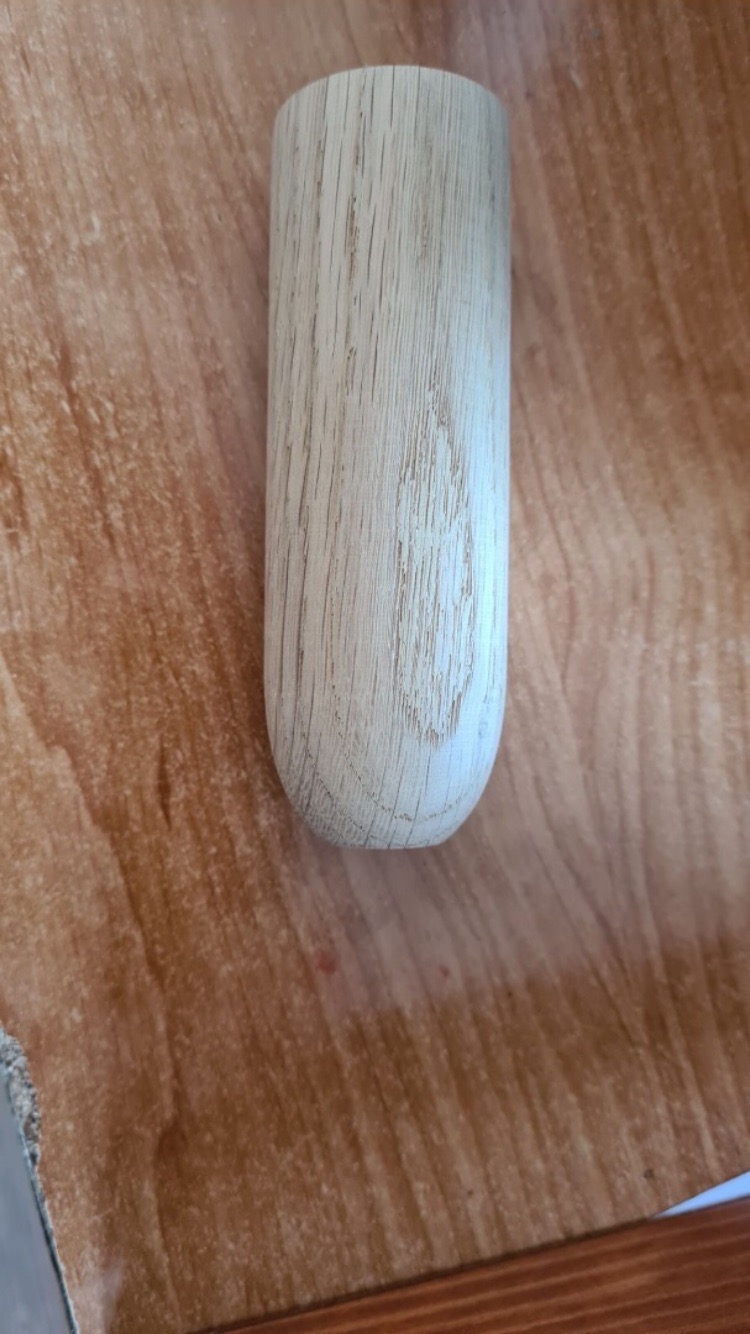 Drewniany, cylindryczny element z zaokrąglonym dnem, leżący na drewnianej powierzchni z widocznym usłojeniem.