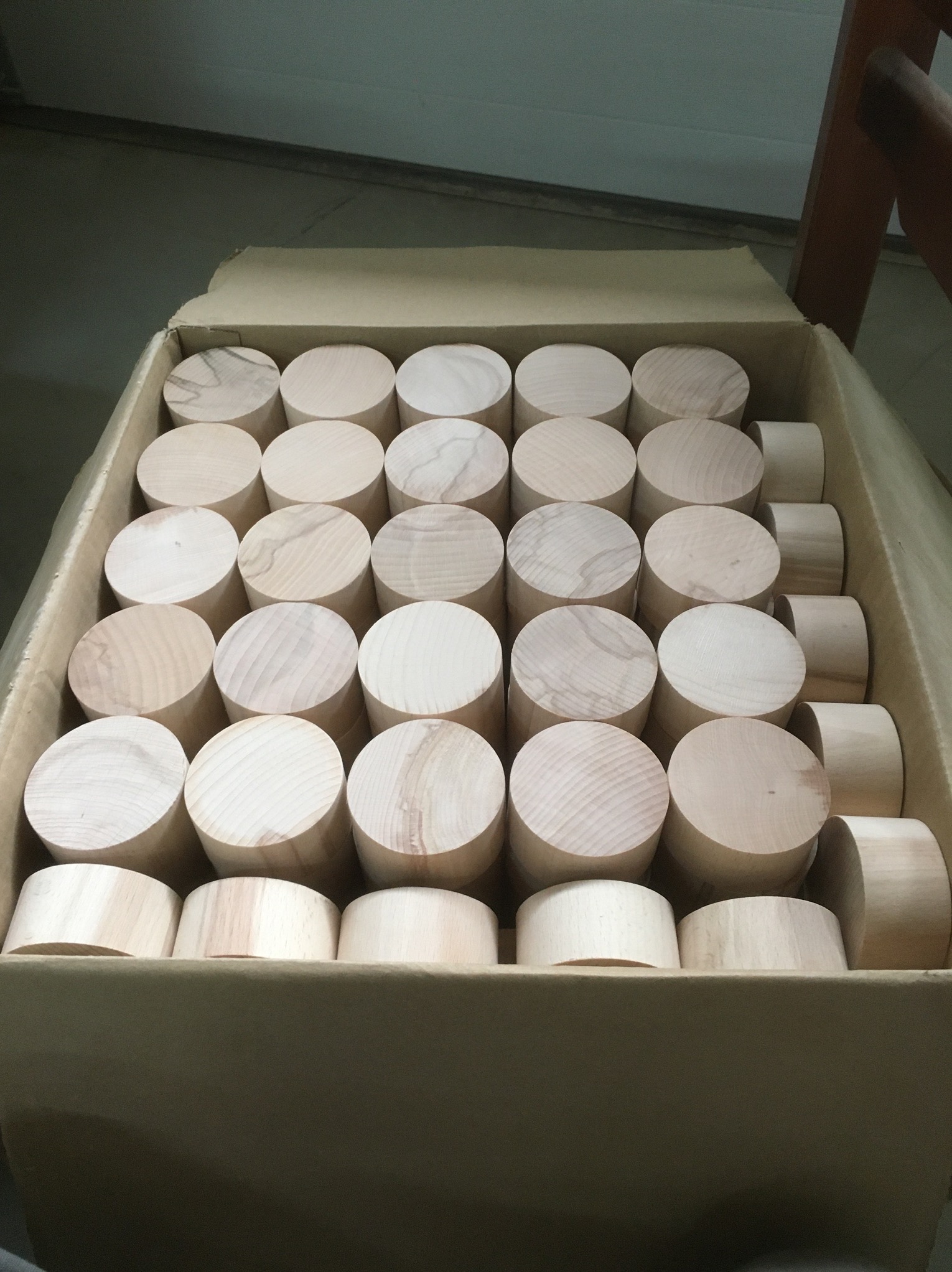 Kartonowe pudło wypełnione okrągłymi, drewnianymi elementami, prawdopodobnie półfabrykatami do dalszej obróbki.