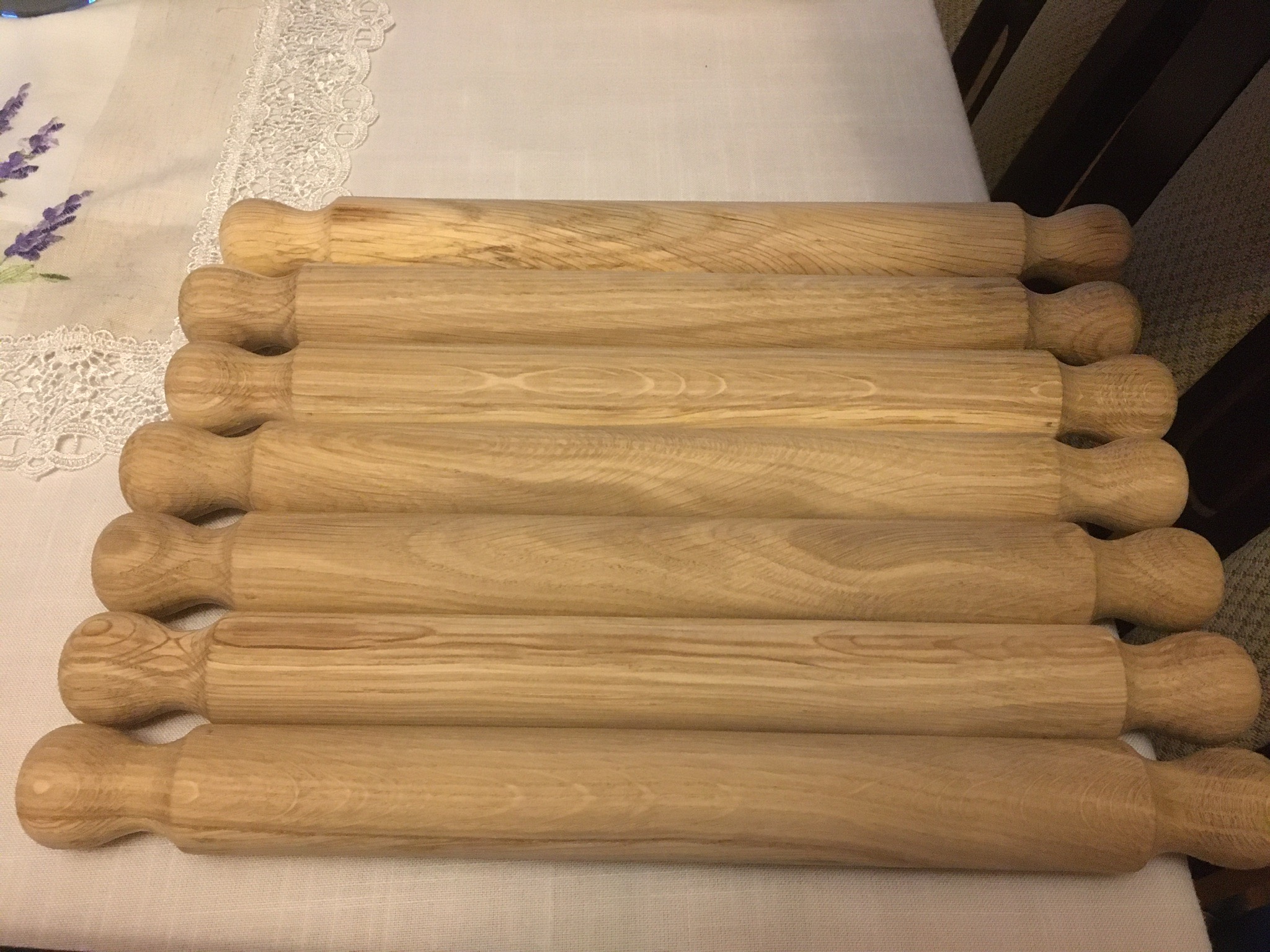 Sześć drewnianych wałków do ciasta ułożonych równolegle na białym obrusie z haftem lawendy.