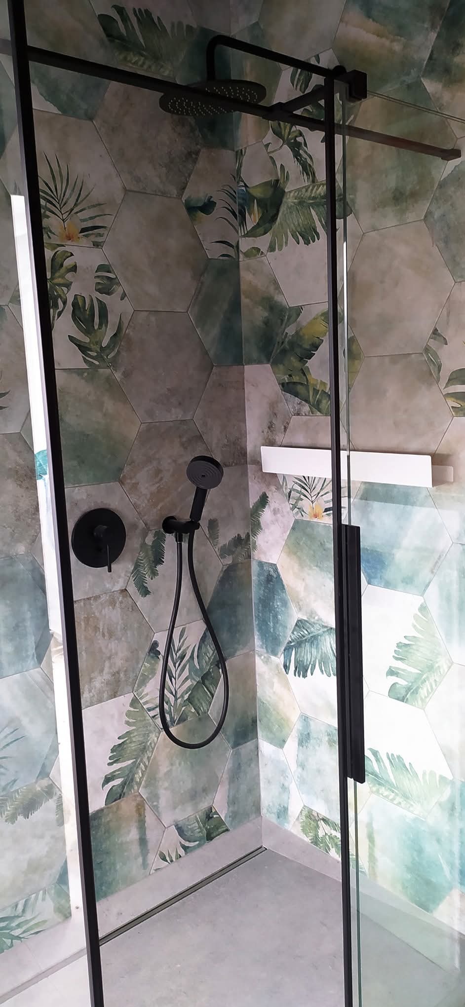 Wykończona kabina prysznicowa z czarną armaturą i heksagonalnymi płytkami w tropikalne wzory. Nowoczesny design łazienki.