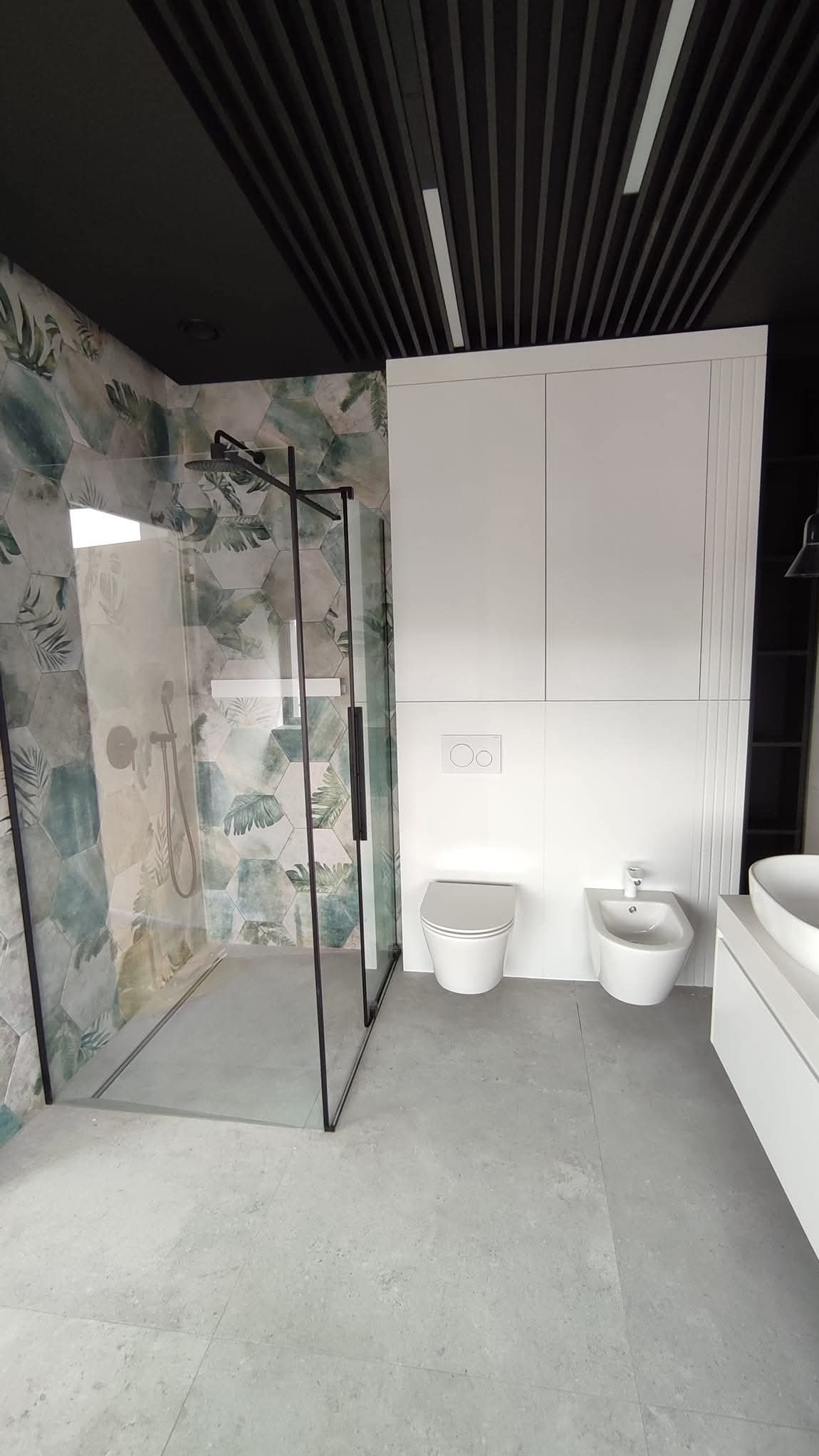 Nowoczesna łazienka w Hutkach z kabiną typu walk-in, heksagonalnymi płytkami w roślinny wzór i czarnym, lamelowym sufitem. Minimalistyczne białe meble.