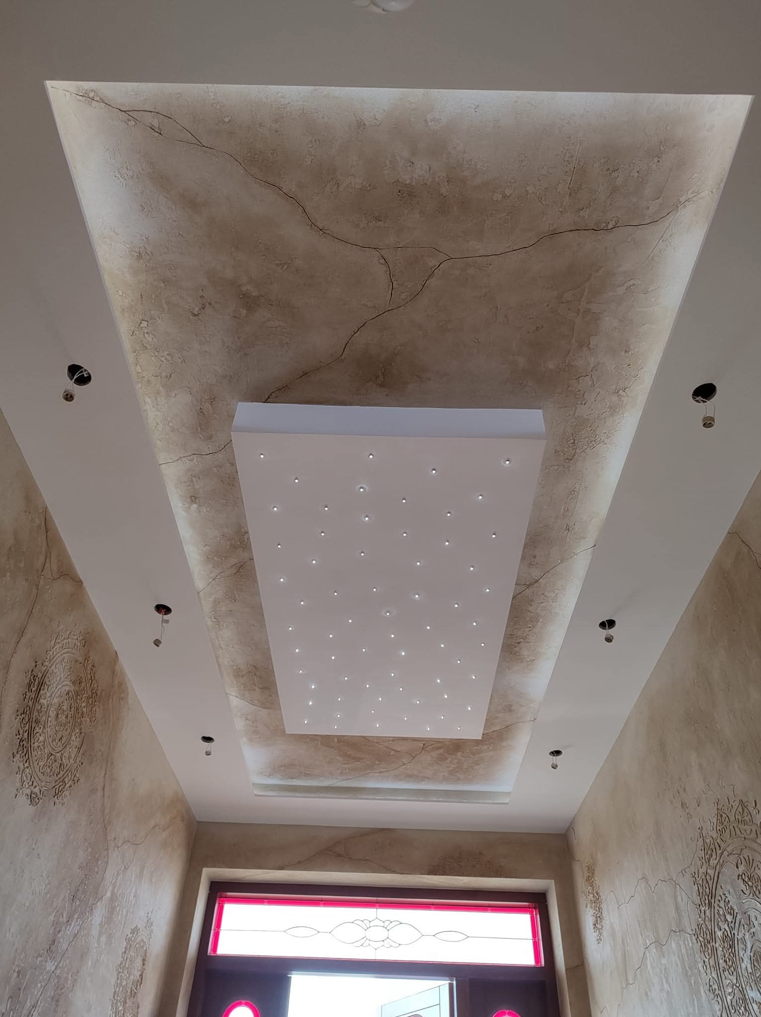 Wykończony sufit z dekoracyjną strukturą imitującą marmur, centralnie umieszczony panel z oświetleniem punktowym LED. Ściany z dekoracyjnymi ornamentami.