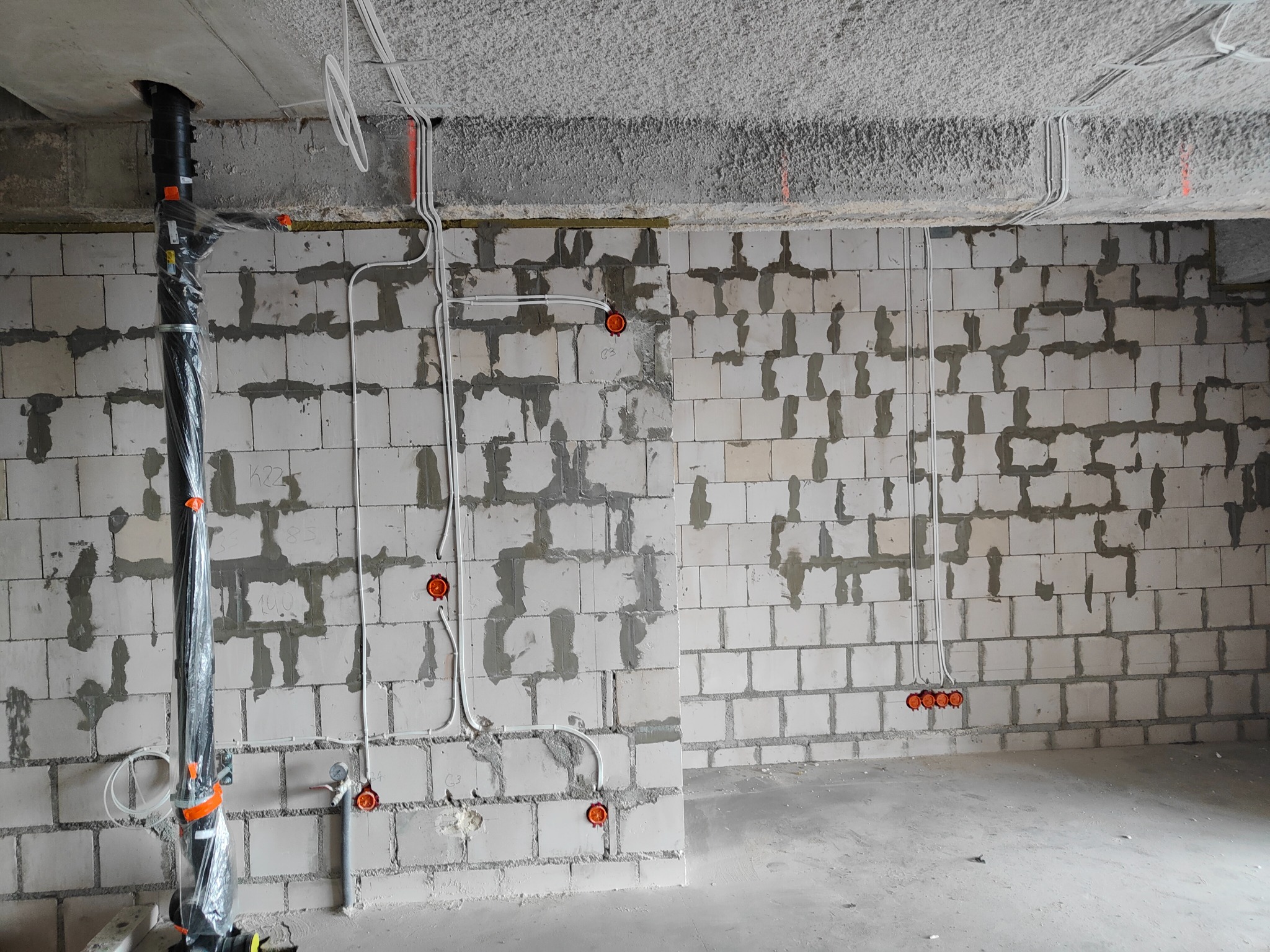 Surowy stan wnętrza w trakcie prac: widoczne przewody elektryczne prowadzone po ścianie z betonu komórkowego, puszki instalacyjne oraz rura kanalizacyjna w folii ochronnej.